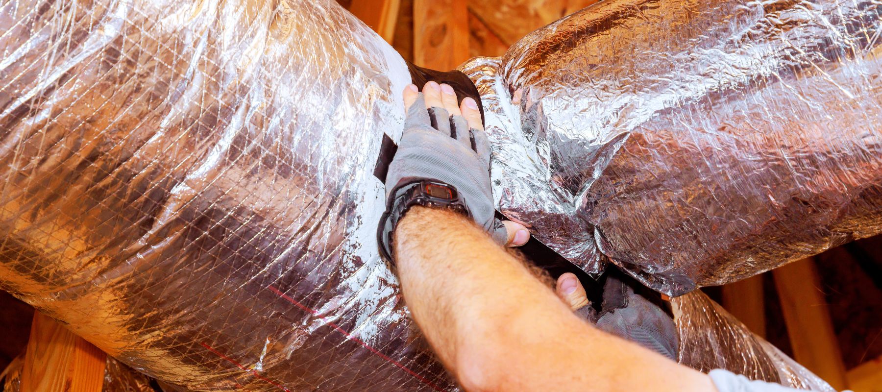 Technician sealing insulated HVAC ductwork in an attic space